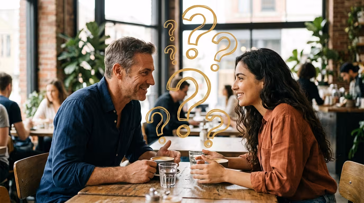 A mature man and a young woman leaning in over coffee, golden question marks floating between them